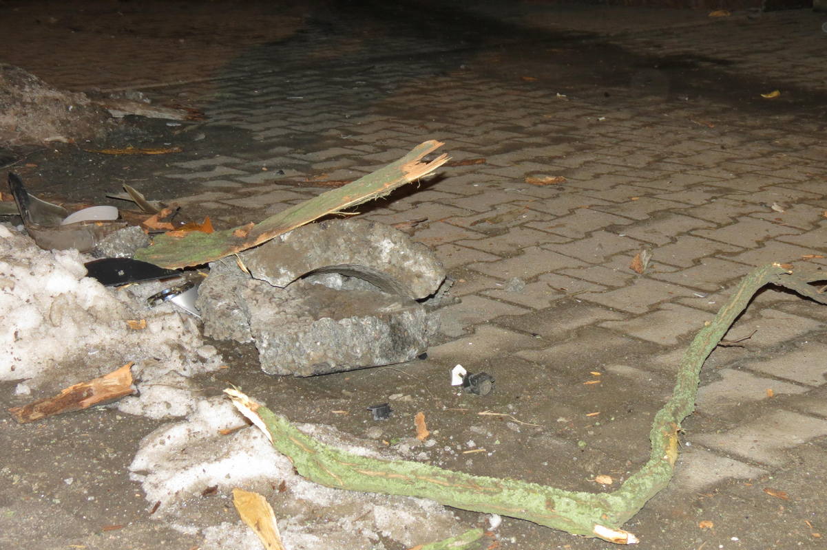 Остатки бетонной урны, пластиковые детали машины и ветки дерева разбросаны по тротуару